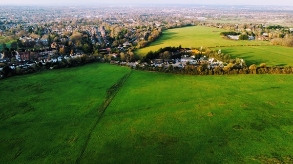 Aerial view of lush green fields with suburban houses in the background.